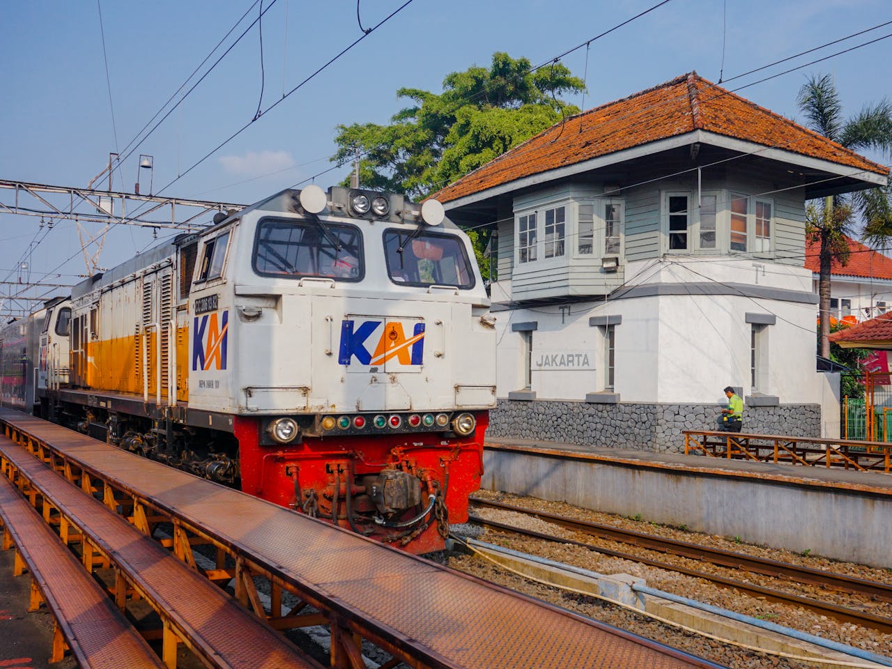 Features A commuter train arrives at a station in Jakarta, Indonesia, with a sign visible.