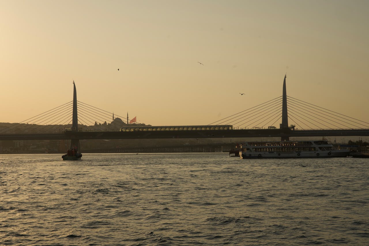 Features Serene sunset over Istanbuls HaliƧ Metro Bridge with boats passing by.